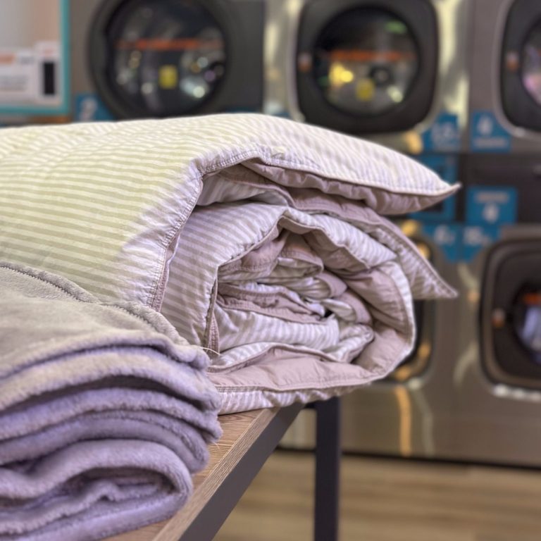 Mantas enrolladas sobre una mesa, con lavadoras de autoservicio de fondo.