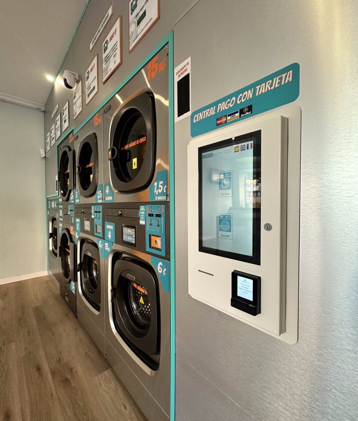 Lavandería de autoservicio con máquinas de lavadoras y secadoras y un panel digital de pago con tarjeta.